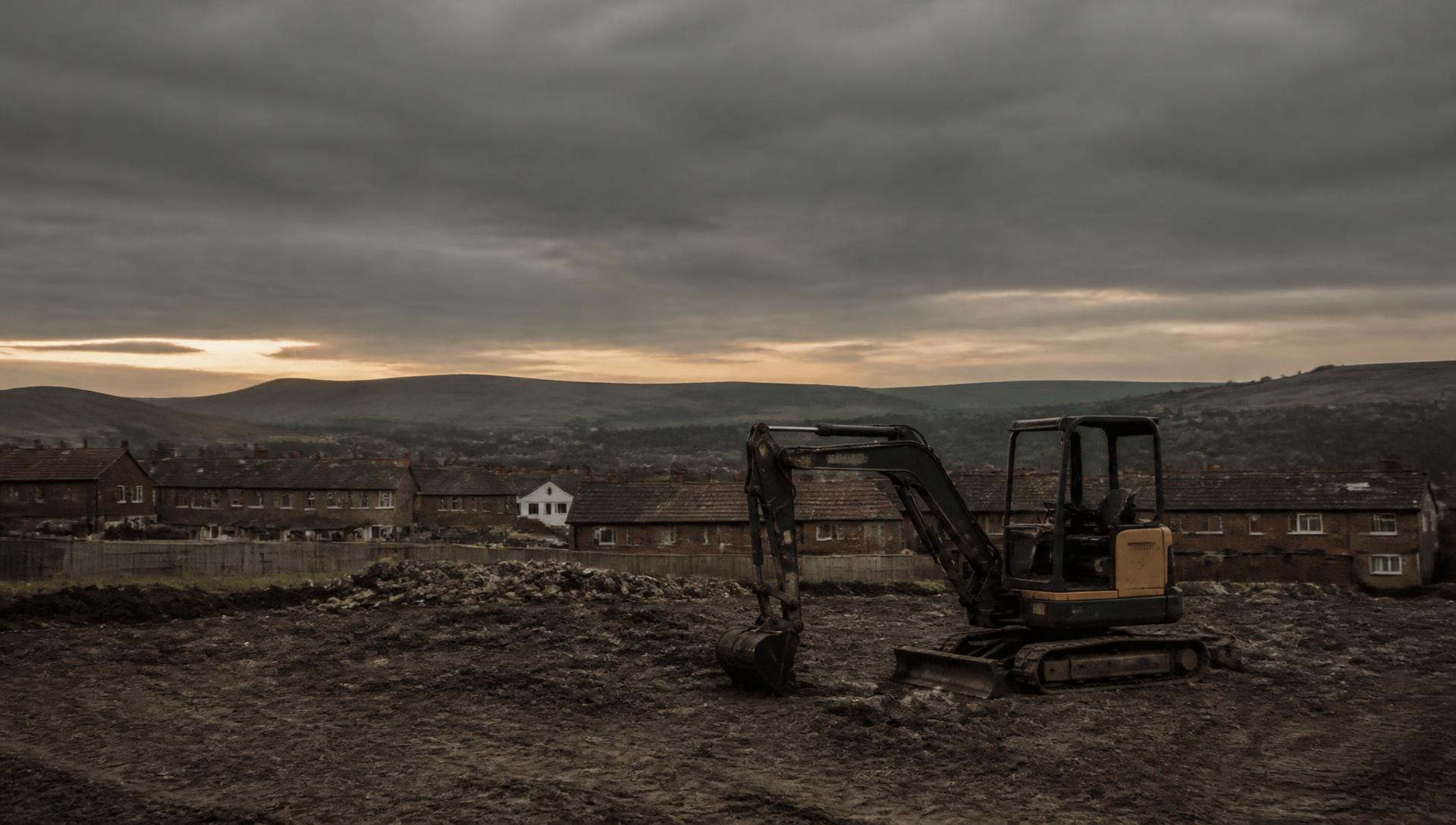 Compact excavator standing on cleared ground above rooftops in the North East of England
